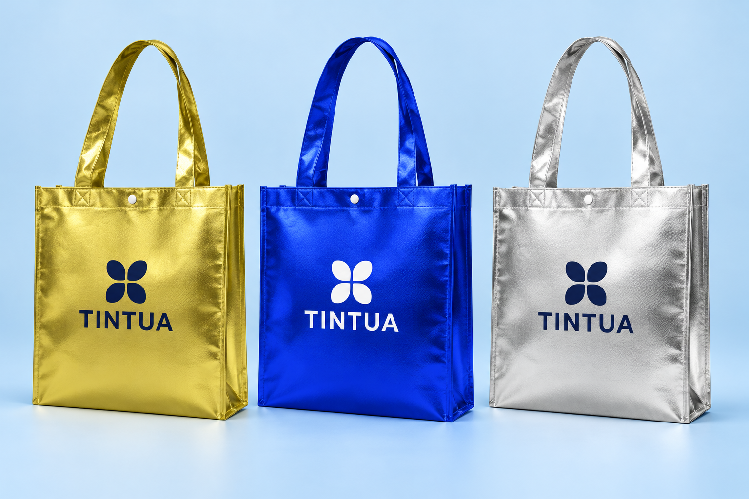 Sacolas de TNT metalizado dourada, azul e prata, com estampa TINTUA e alças compridas, referências ilustrativas