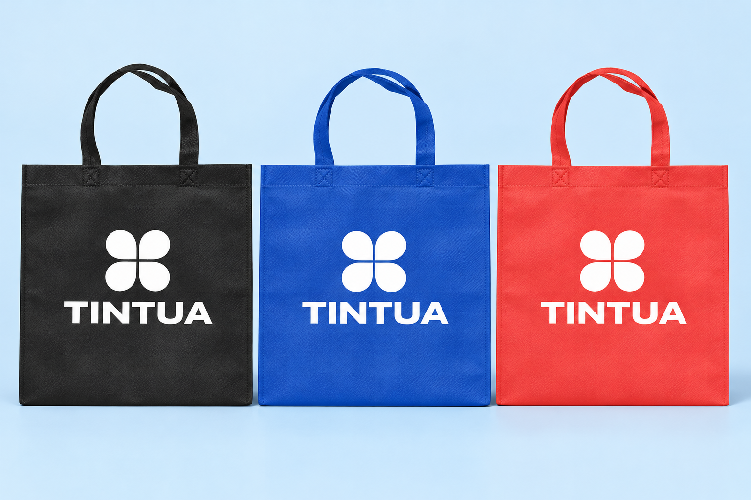 Sacolas TNT foscas preta, azul e vermelha, modelo simples com alças de tecido e estampa TINTUA, referências ilustrativas